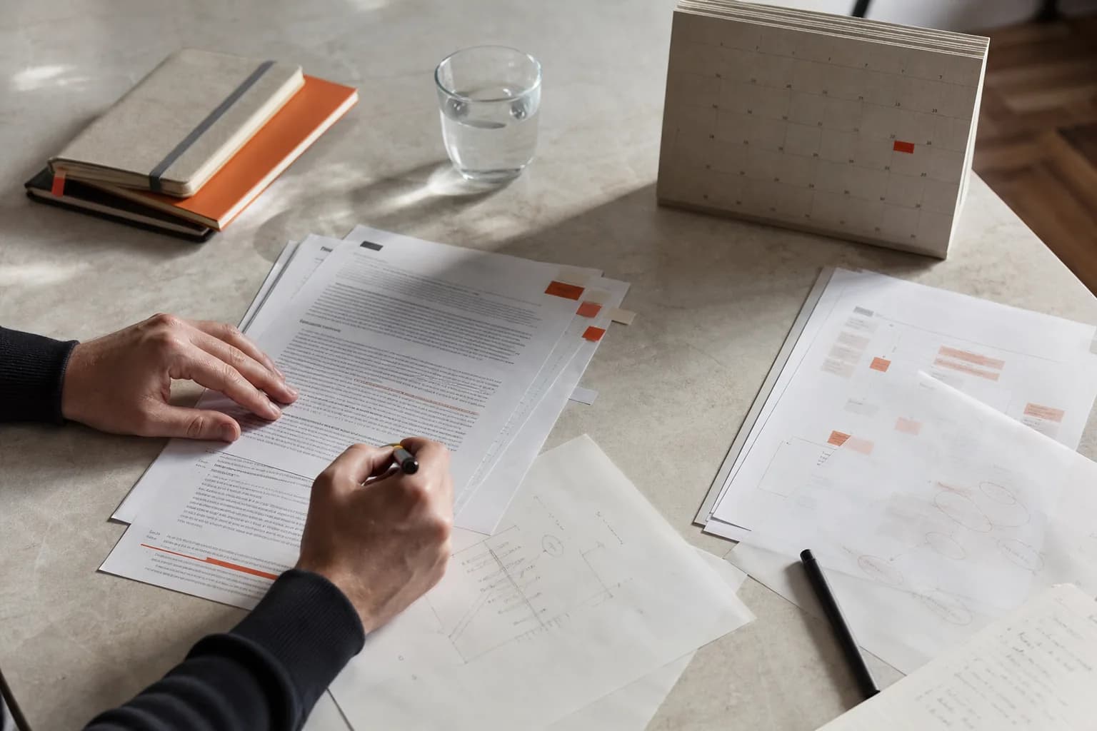 Mãos a rever documentos e um calendário numa mesa de trabalho